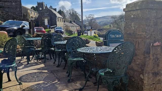 Quaint outdoor seating with green chairs and tables at Muker Village Store & Teashop, set against a scenic backdrop.