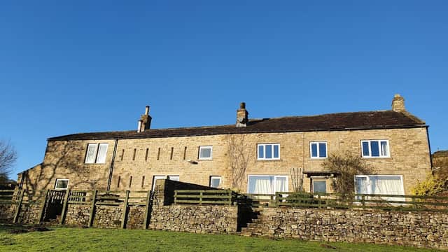 Stone farmhouse with multiple windows and a grassy foreground, set against a clear blue sky in Yorkshire.