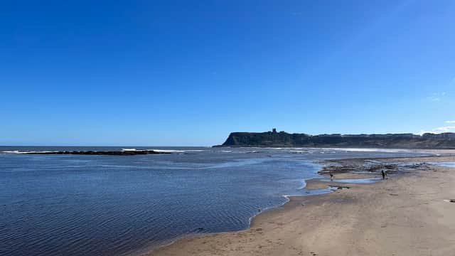 Scenic view of Scalby Mills beach, with calm waters and a clear blue sky, framed by rugged cliffs in the distance.