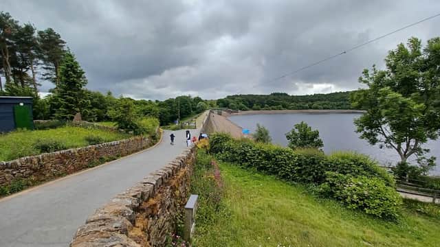 Scenic view of Ogden Water with a dam, pathway, lush greenery, and cloudy sky in Mixenden, Yorkshire.