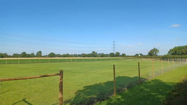 Spacious fenced dog park with lush green grass, clear blue sky, and distant trees in Wilberfoss, Yorkshire.