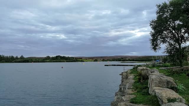 Calm lake with rocky shore, cloudy sky, and distant hills in Scaling, North Yorkshire.