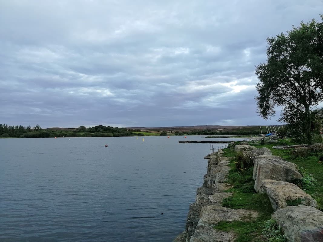 Calm lake with rocky shore, cloudy sky, and distant hills in Scaling, North Yorkshire.