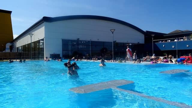 Sunny day at Alpamare UK, featuring a large outdoor pool with swimmers and sunbathers enjoying the water.