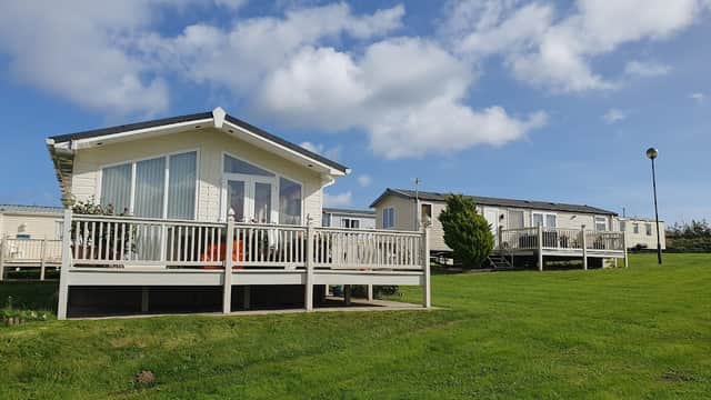 Two holiday cabins with wooden decks on a grassy area, under a blue sky with fluffy clouds at Haven Blue Dolphin Touring Site.