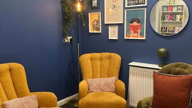 Cozy reading nook with yellow armchairs, green chair, colorful artwork, and a patterned rug against a blue wall.