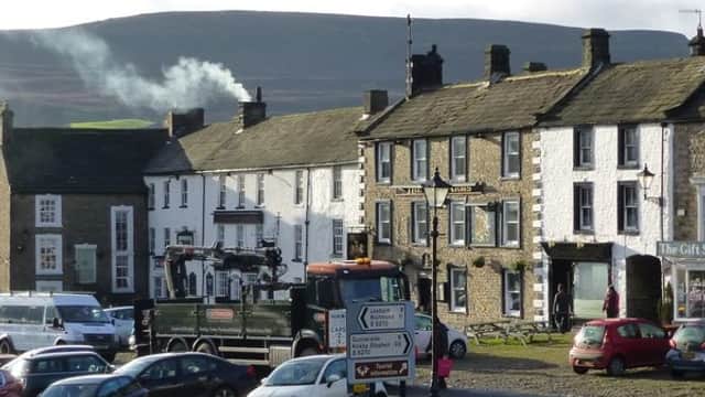 Historic stone buildings of Low Row Bunk Barns, surrounded by parked cars and rolling hills in the background.