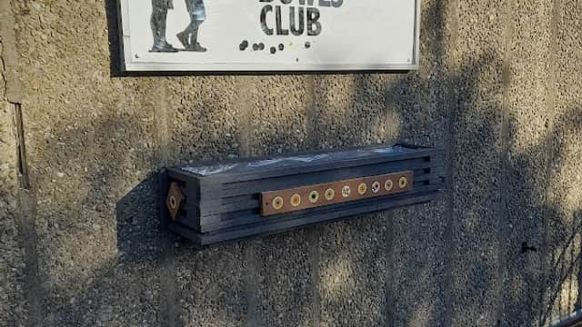 Sign for Nafferton Bowls Club on a textured wall, with a wooden score board beneath it.