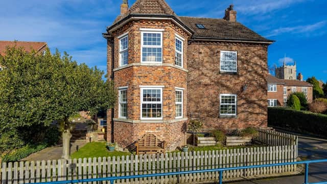 Charming brick boutique B&B with large windows, a garden bench, and a picket fence under a clear blue sky.