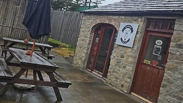 Stone building with wooden picnic tables outside, an umbrella, and a sign for "The Manor Farm Cafe" in Bellerby.