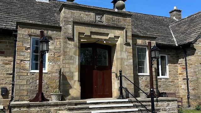 Stone entrance with steps, decorative lanterns, and a clear blue sky above Grantley Village Hall in Yorkshire.