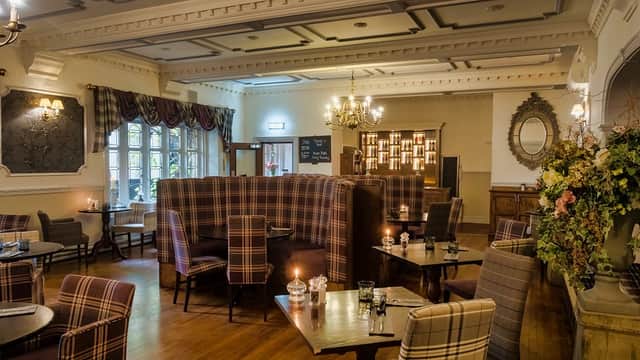 Elegant dining area with plaid seating, wooden tables, chandeliers, and floral arrangements in a cozy atmosphere.