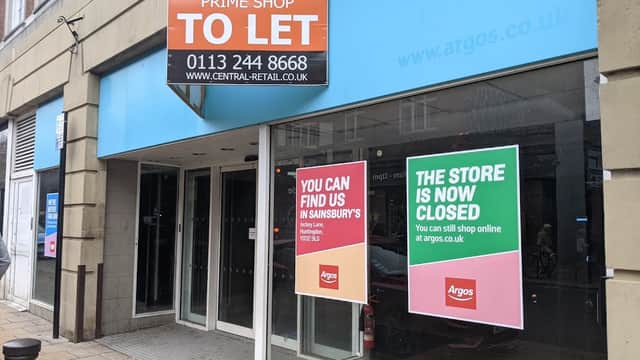 Closed storefront with "TO LET" sign and notices for Sainsbury's and Argos, featuring large glass windows.