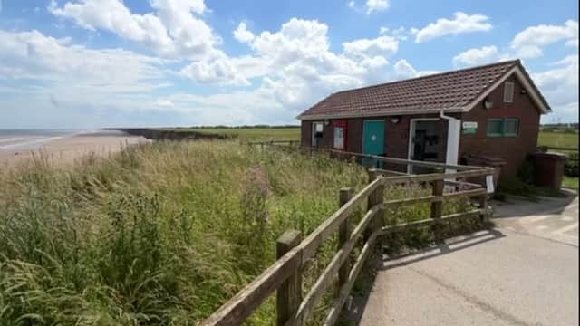 Pay & Display parking area near Mappleton Beach, with a small building and grassy surroundings under a blue sky.