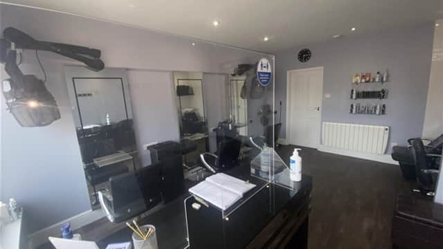 Modern hair studio with styling chairs, mirrors, and a reception desk featuring health safety signage.