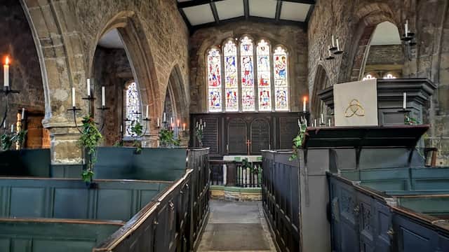 Interior of Holy Trinity Church featuring stained glass windows, stone walls, pews, and candlelit ambiance.
