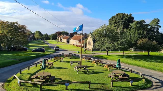 The Horseshoe Inn features a grassy area with picnic tables, a flagpole, and surrounding trees in a quaint village setting.