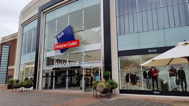 Entrance to Designer Outlet York with large glass windows, "Welcome" sign, and displayed clothing on mannequins.