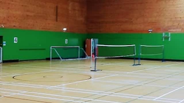 Indoor sports hall with wooden walls, green accents, and badminton nets set up on a wooden floor.