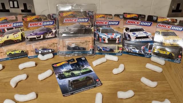 Hot Wheels cars in packaging displayed on a wooden surface, surrounded by packing peanuts.