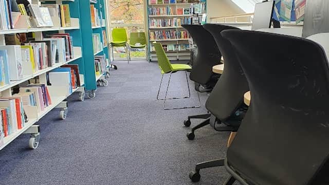Bright library interior with bookshelves, chairs, and large windows letting in natural light.