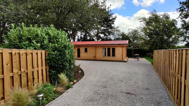 Wooden lodge with red roof surrounded by greenery and gravel pathway, under a partly cloudy sky in Huby, Yorkshire.