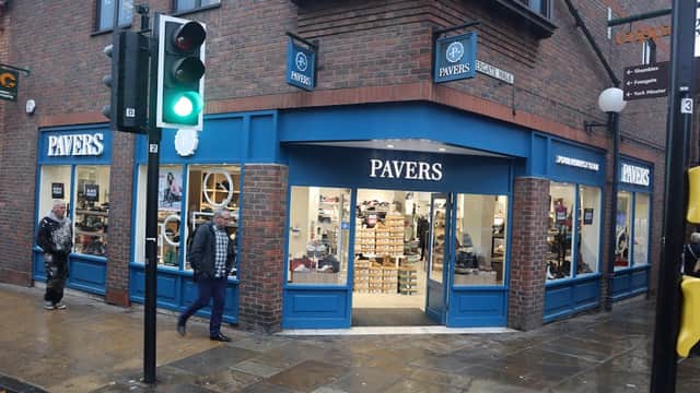 Pavers Shoes storefront with blue accents, large windows displaying shoes, and pedestrians outside in York, Yorkshire.