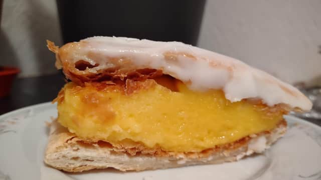 A slice of pastry topped with icing, revealing a creamy yellow filling, served on a decorative plate.