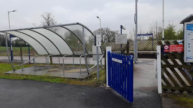 Bus stop shelter with a blue gate, signposts, and a grassy area in Long Preston, Yorkshire, under a cloudy sky.