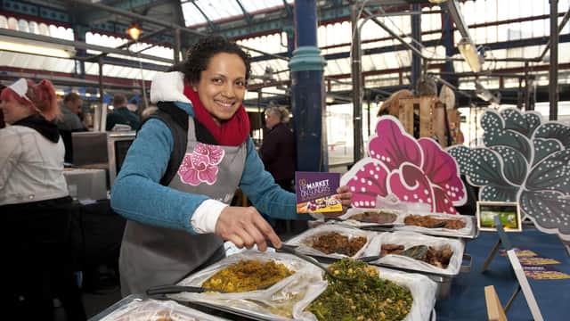 Vendor serving diverse dishes at a bustling indoor market with decorative stalls and overhead glass panels.