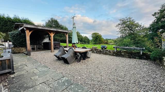 Outdoor seating area with a wooden pergola, gravel surface, and lush greenery in the background.