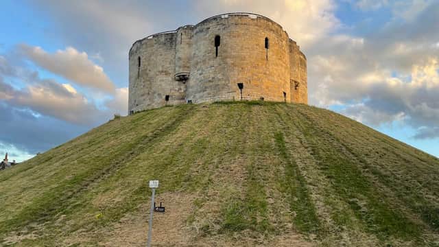 Castle on a grassy mound under a cloudy sky, with a car park and parking lines in the foreground.