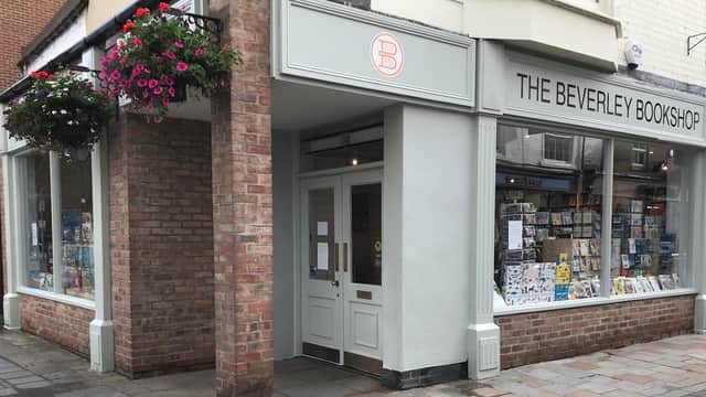 Charming brick storefront with large windows displaying books, colorful hanging flowers, and a welcoming entrance.