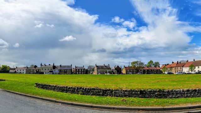 A panoramic view of The Green in Ellerton-on-Swale, featuring cottages, a grassy area, and a blue sky with clouds.