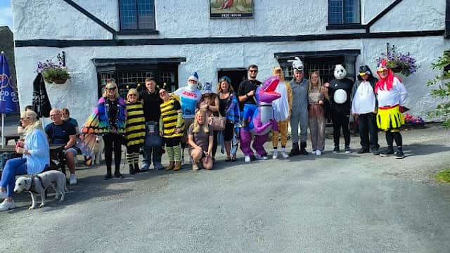 Group of people in colorful costumes outside Pheasant Inn & Caravan Park, with a clear blue sky and flowers.