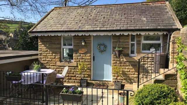 Charming stone cottage with a blue door, flower wreath, patio table, and garden under a clear blue sky.