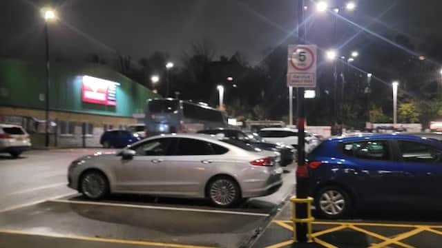 Pay & Display parking area in Brighouse, Yorkshire, with silver and blue cars under bright lights at night.