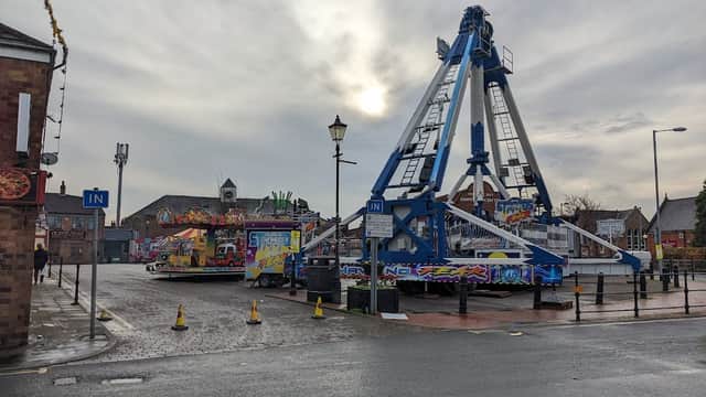 Ferris wheel and colorful fairground rides in a car park, with cloudy sky and street lamps in Driffield, Yorkshire.