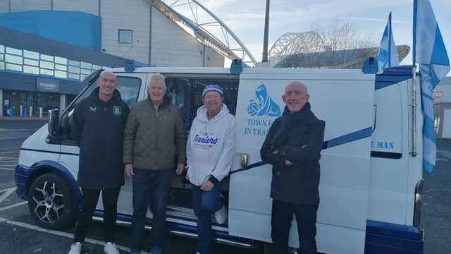 Four men stand next to a van decorated with flags in a car park near a stadium in Huddersfield, Yorkshire.