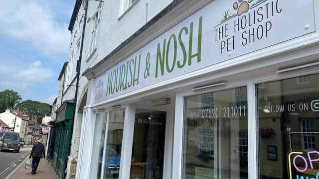 Sign for "Nourish & Nosh", a holistic pet shop, with a paw print logo, located in a charming street in Harrogate.