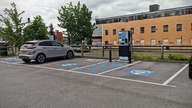 Pay & Display car park with a grey car, blue disabled parking spaces, and a payment machine against a modern building.