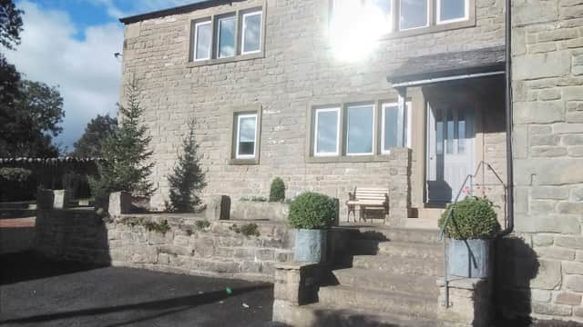 Stone exterior of Valleymead Guest House with steps, potted plants, and a wooden bench under a sunny sky.