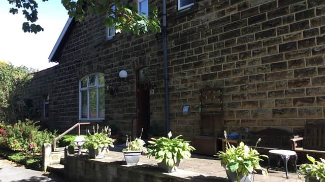 Stone exterior of The Firs Guesthouse with potted plants and a wooden bench on a sunny day in Hinderwell, Yorkshire.