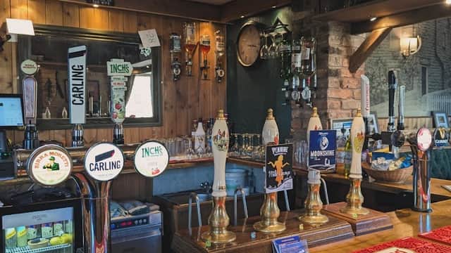 Bar counter with various beer taps, a mirror, and shelves displaying drinks in a rustic setting.