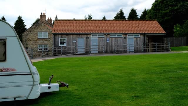 Wooden building with three doors, grassy area, and a caravan in the foreground, set in a rural Yorkshire landscape.