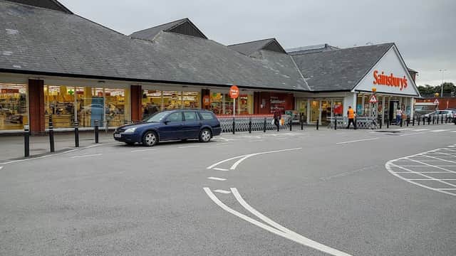 Sainsbury's Petrol Station with a gray car parked outside, surrounded by a spacious parking lot and a cloudy sky.