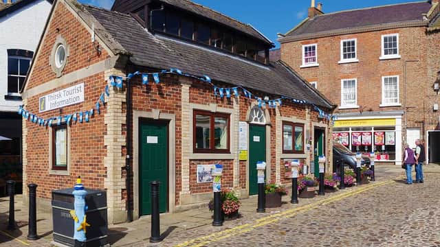 Brick building with green doors, bunting, and flower pots, located in a cobbled street in Thirsk, Yorkshire.