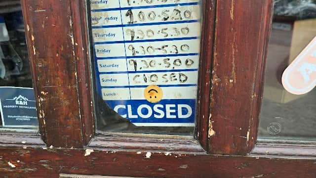 Business hours sign on a wooden door, showing opening times and a "CLOSED" notice.