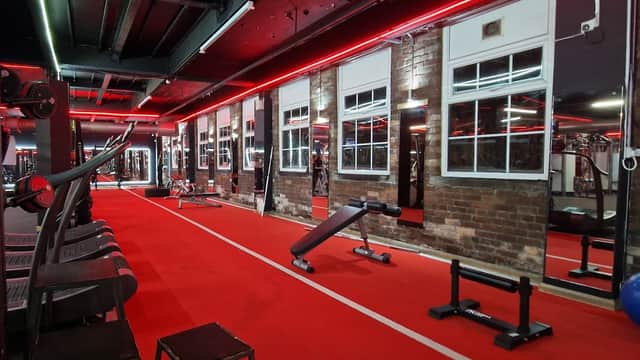 Modern gym interior with red lighting, exposed brick walls, workout equipment, and a vibrant red carpeted floor.