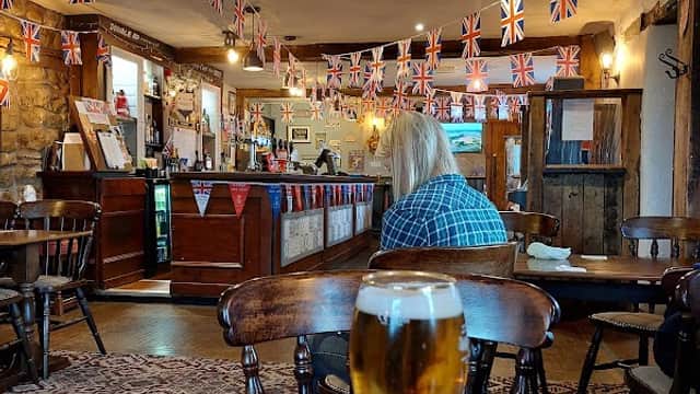 Interior of Poachers Barn bar with Union Jack bunting, wooden furniture, and a glass of beer on a table.